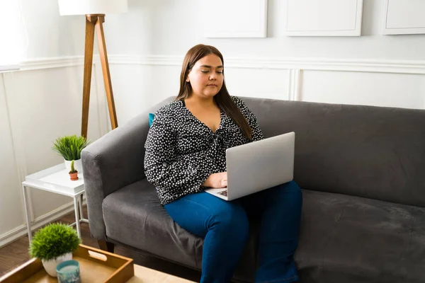 拉丁美洲肥胖妇女在笔记本电脑上打字 在家工作 客厅里的自由职业加身材女人 — 图库照片
