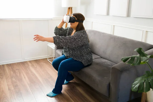 Plus size woman wearing VR glasses and playing virtual reality video games at home. Curvy woman using immersive technology