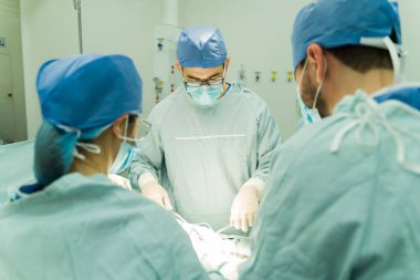 Kendine güvenen erkek cerrah zor bir ameliyatla bir hastanın hayatını kurtarıyor. Ameliyathanede tıbbi personel var. 