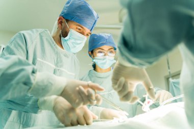 Kadın cerrah ve doktor yüz maskesi takıyor ve ameliyat aletlerini ameliyathanede kullanıyor.