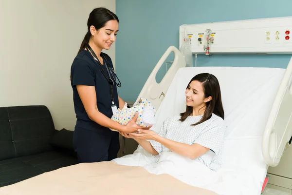 漂亮而快乐的护士带着新生儿到医院病床上休息的一位兴奋的新妈妈那里 — 图库照片