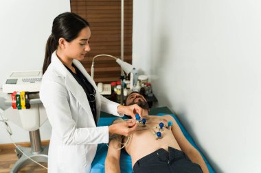 Kadın kardiyolog elektrokardiyogram testi yapıyor. Kalp rahatsızlığı olan hasta bir adam kalp atışlarını kontrol ettiriyor.