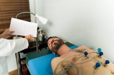 Kalp atış hızını kardiyolog muayenehanesinde elektrokardiyogram cihazıyla izleyen Latin bir adam.