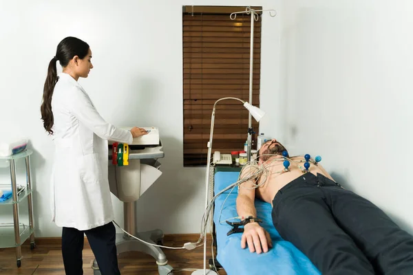 拉丁女医生和男青年收到心电图报告患心脏病的男性患者 — 图库照片
