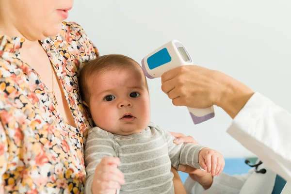 小児科医のオフィスで熱で病気のかわいい赤ちゃん 病気の新生児に赤外線温度計を使う医者 — ストック写真