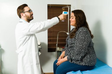 Temas etmeyen bir lazer termometreyle ateşini ya da ofisteki mutlu bir hastada virüs olup olmadığını kontrol eden gülümseyen bir doktor.