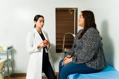 Çekici genç beslenme uzmanı şişman bir hastayla kalp sorunlarını önlemek için sağlıklı bir diyet hakkında konuşuyor.