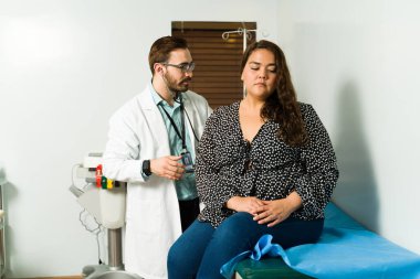 Çekici bir doktor, hasta ve obez bir kadının ciğerlerini kontrol etmek için stetoskobu kullanıyor.