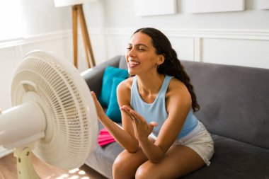 Güzel Latin kadın elektrikli yelpazeyi açtıktan sonra heyecanlanıyor ve sıcak havadan dolayı havanın tadını çıkarıyor.