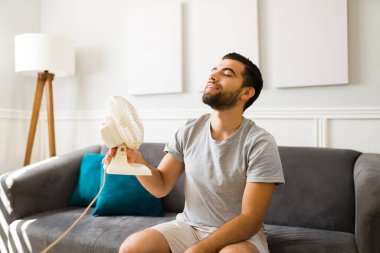 Rahatlamış genç adam eve geldikten sonra hayran havasının tadını çıkarıyor. Latin adam yazın elektrikli yelpaze açıyor.