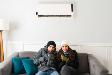 Portrait of an attractive hispanic couple cooling at home and feeling cold with the ac unit on