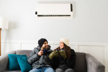 Happy woman and man laughing while drinking coffee in the living room while enjoying the air conditioning air during the summer