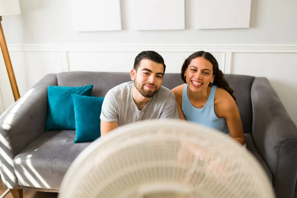 Attractive Smiling Couple Enjoying Air Electric Fan Cooling Because Warm — стоковое фото