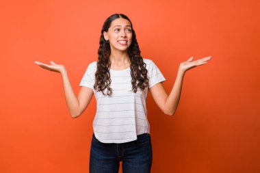 Güzel bir kadının, kafası karışmış bir ifadeyle omuzlarını silkerken, şüpheleri olan bir stüdyo fotoğrafı.