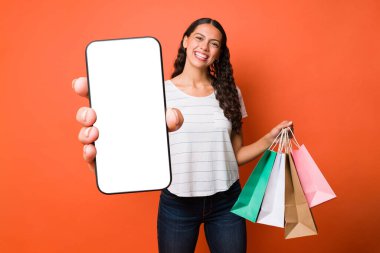 Güzel genç bir kadın akıllı telefonuyla online alışveriş yapıyor ve internet uygulaması ile para biriktiriyor. 