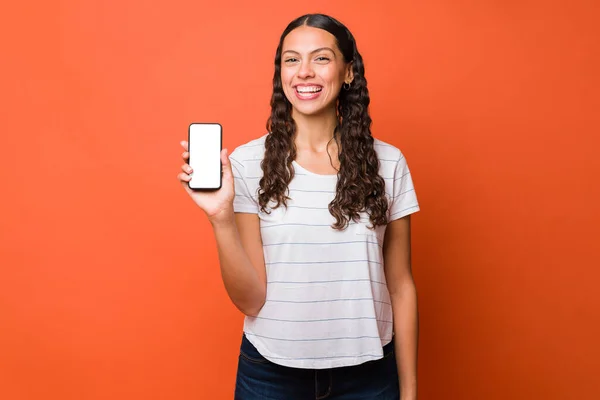 一个20多岁的女人笑着看着相机 同时用一个新的应用程序展示她的智能手机的肖像 — 图库照片