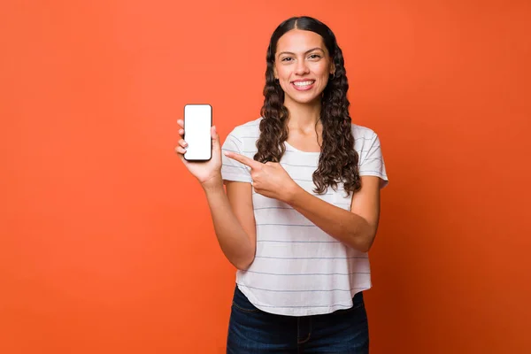 Glimlachende Spaanse Jonge Vrouw Wijst Naar Haar Smartphone Tijdens Het — Stockfoto
