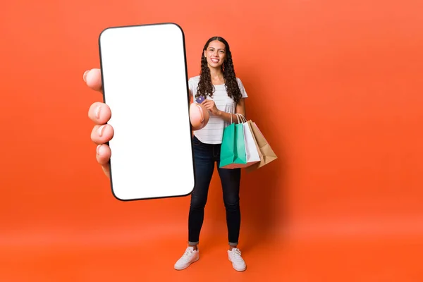 迷人的拉丁女人在网上购物和使用信用卡时 会出现一个白色屏幕的大尺寸智能手机 — 图库照片