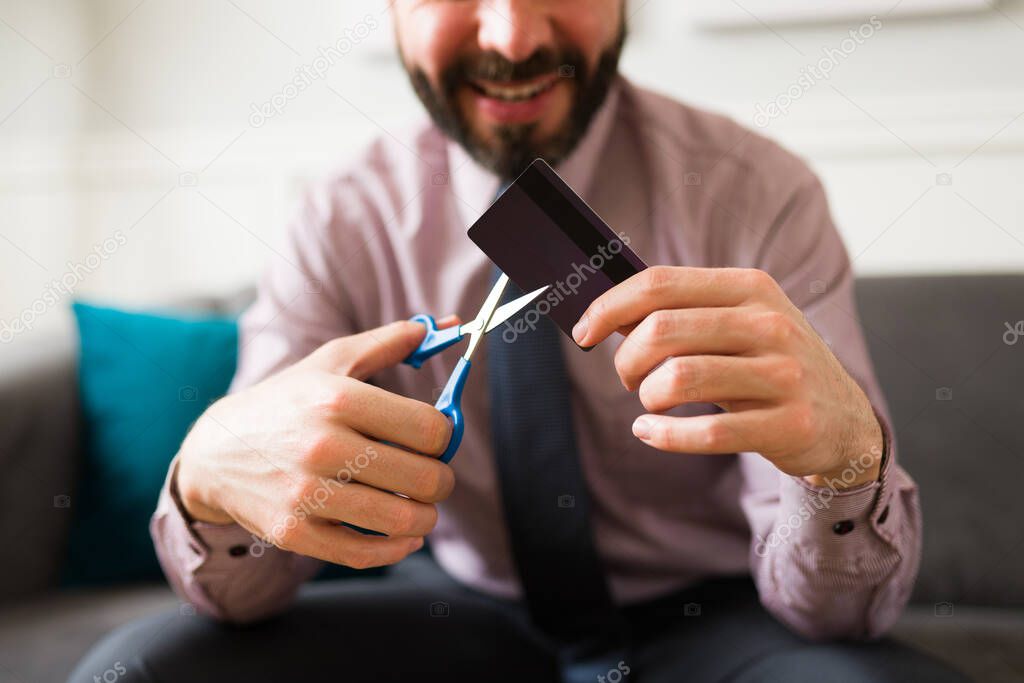 Close up of a happy rich man cutting with scissors his credit card after reaching financial freedom