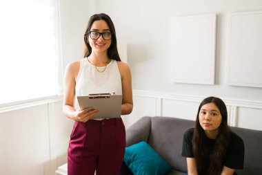 Üzgün genç bir kızla terapi seansı yaparken gülümseyen ve kameraya bakan güzel bir kadın terapist. 