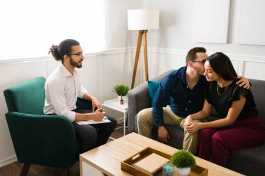 Çekici bir koca, bir terapistle evlilik sorunlarını çözmeye çalışırken karısını öpüyor.