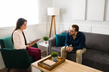 30 'lu yaşlarda bir erkek hastayla terapi seansında ruh sağlığı sorunları hakkında notlar alan güzel bir psikolog.