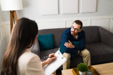 Depresyonda olan üzgün bir adam koltukta oturup ofisteki profesyonel bir terapistle duygusal sorunlarını konuşuyor.