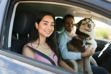 Arabada köpeğiyle gülümseyen ve yolculuğa hazır neşeli bir İspanyol çiftin portresi.