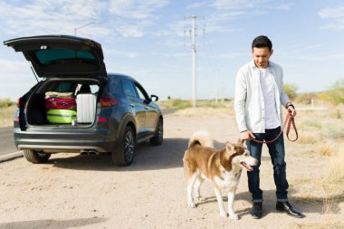Yakışıklı Latin bir adam yol kenarında köpeğini tasmasıyla gezintiye çıkarıyor.