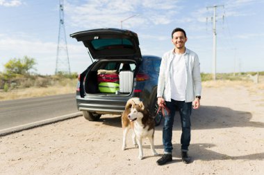 Çekici bir delikanlının, köpeğini bir araba yolculuğu sırasında yol kenarında yürüyüşe çıkarması.
