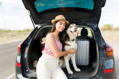 Beautiful young woman looking at the camera while enjoying some time with her dog on a car trip