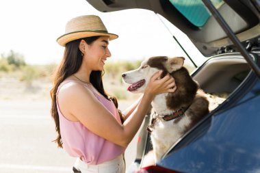 Beautiful young woman petting her husky dog while stopping the car at the side of the road 