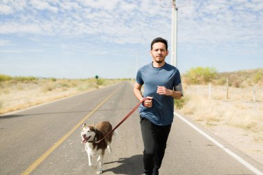 İri köpeğiyle yolda koşan azimli bir genç adam. Latin adam dışarıda egzersiz yapıyor.