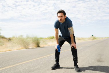 Yorgun ve susamış bir adam güneşli bir günde uzun bir koşudan sonra su içiyor.