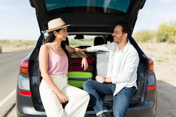 Neşeli çift bir tatil sırasında yol kenarındaki araba bagajında dinleniyor.