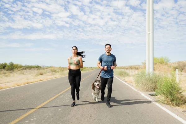 Fitness young couple running together outdoors with their active husky dog