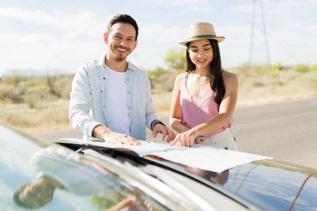 Beautiful latin woman and happy young man checking a road map while driving for a vacation trip