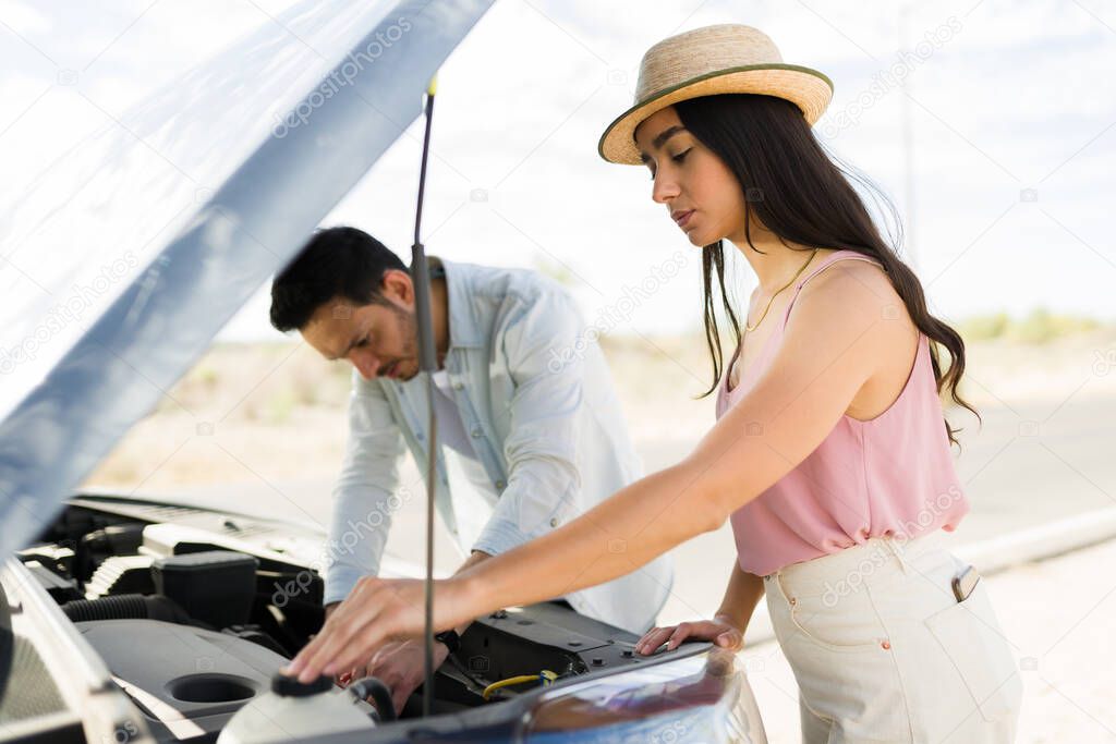 Upset young woman and man checking the engine after the car broke down during a road trip