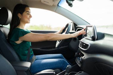Excited young woman using the GPS in her car to get directions and listening to music on the radio 