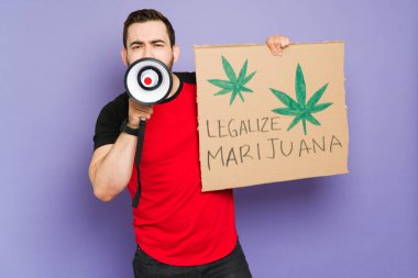 Protesto sırasında megafon kullanan erkek protestocu, elinde marihuana mesajını yasallaştıran bir pankart tutuyor.