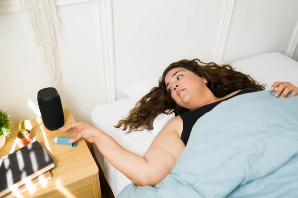 一位忧心忡忡的肥胖女人躺在床上 因哮喘发作而寻找吸入器的头像 — 图库照片