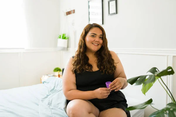 一个快乐而肥胖的女人在她的卧室里拿着一只月经杯微笑的画像 — 图库照片