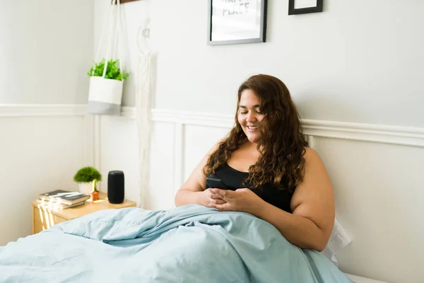 早上躺在被窝里 一边笑一边用智能手机发短信 快乐肥胖的女人 — 图库照片