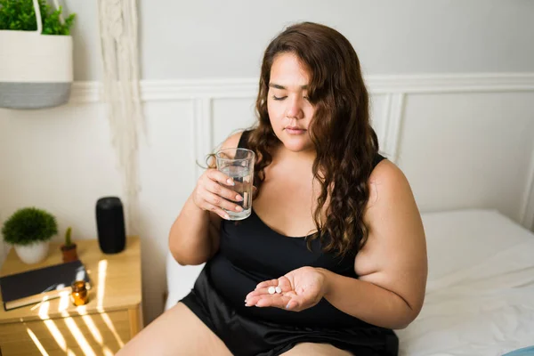 Healthy obese woman taking vitamins to feel better during the morning. Sick woman taking pills in bed