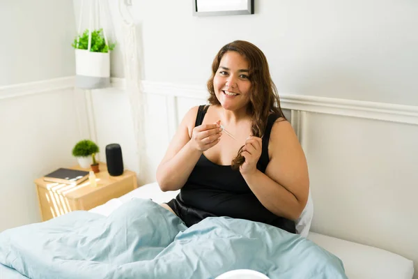 Happy obese woman in bed with damaged hair putting repairing oil and a treatment for a shiny beautiful hair