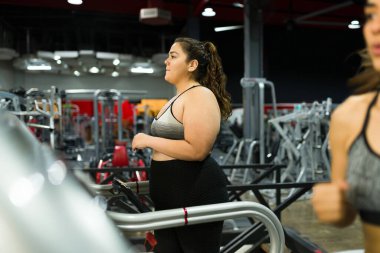 Koşu bandında koşan ve kilo vermek için diyet planı yapan aktif ve geniş beden giyimli bir kadın.