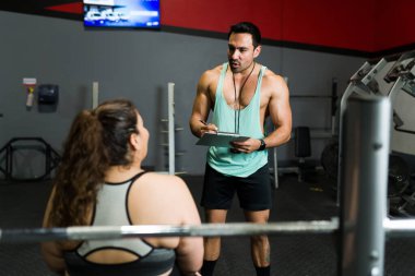 Spor salonundaki şişman genç bir kadına egzersiz rutini ve diyet planı uyguluyor.