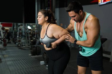 Çekici kişisel antrenör spor salonundaki egzersiz sırasında şişman genç bir kadına yardım ediyor. 