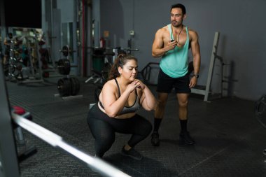 Etkin şişman kadın çömelme egzersizleri yapıyor. Ayrıca spor salonunda spor salonunda spor yapan kilolu bir kadın kilo vermek için spor yapıyor.