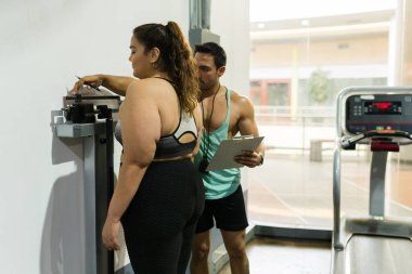 Kişisel antrenör şişman Latin bir kadının kilo verme yolculuğunu kontrol ediyor. Kilo ölçeğinde şişman bir genç kadın.